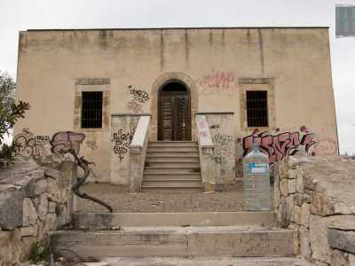 Dopo aver superato profumati alberi di mirto e pitosforo ci imbattiamo in un edificio color ocra, forse il vecchio centro informazioni, con le finestre inferriate e i muri ricoperti da murales, immancabili in un luogo isolato e degradato come questo